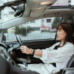 Side view unemotional Asian female in casual white clothes steering right hand drive car along urban streets in daytime